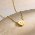 Gros plan sur un collier doré à petit cœur gravé d'une initiale