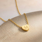 Gros plan sur un collier doré à petit cœur gravé d'une initiale