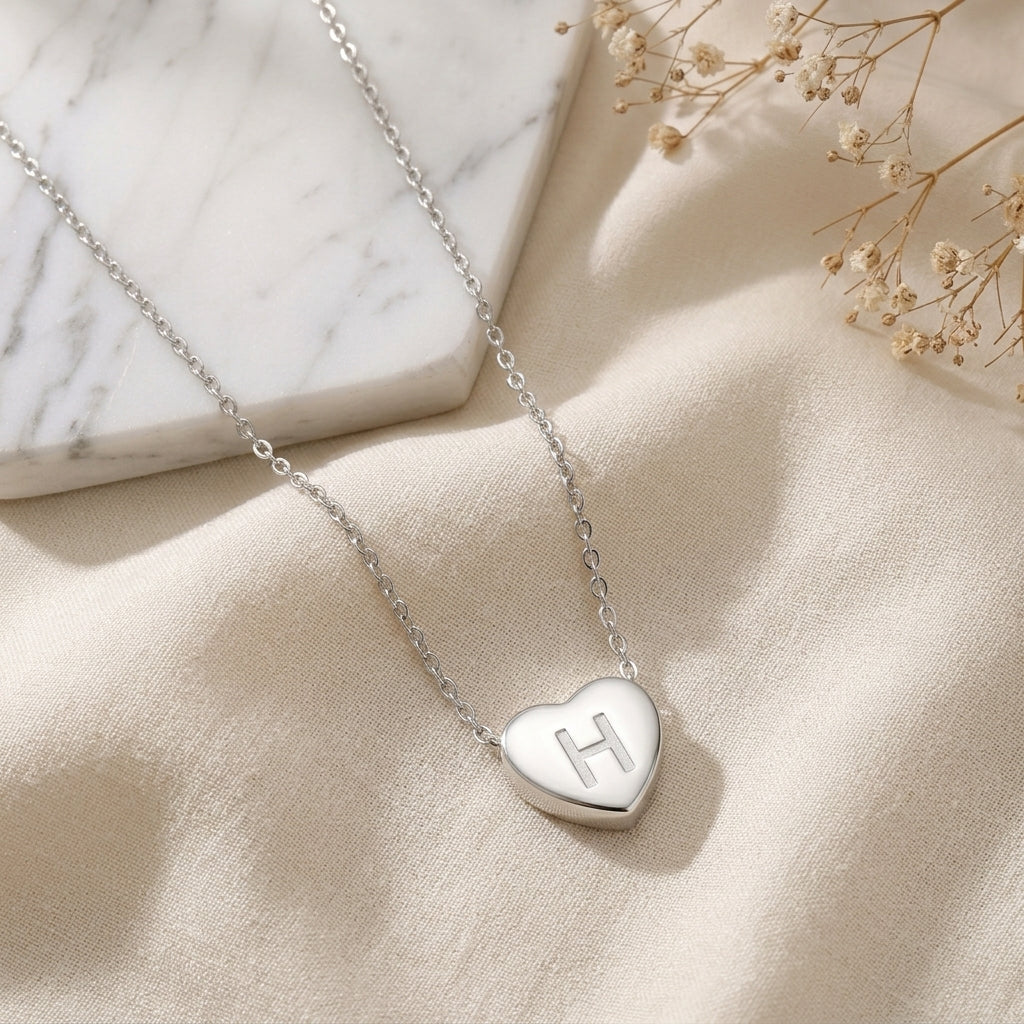 Collier en acier inoxydable à petit cœur gravé d'une initiale, posé à plat