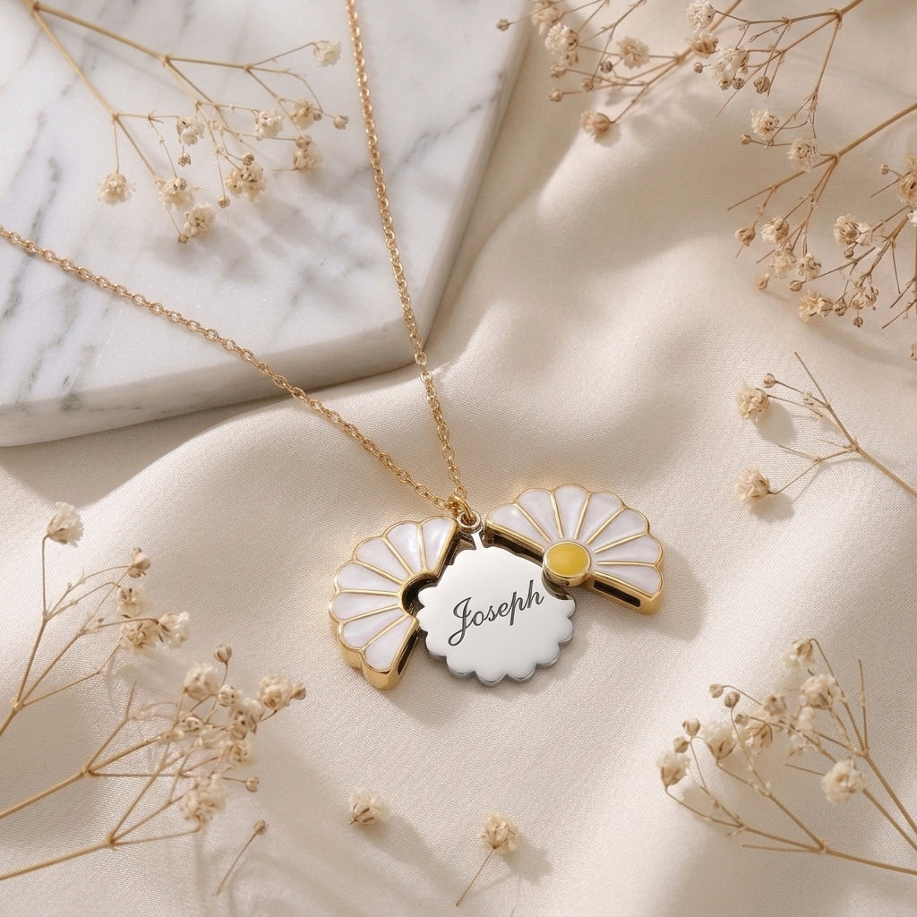 Collier marguerite doré ouvert sur un prénom gravé, posé à plat