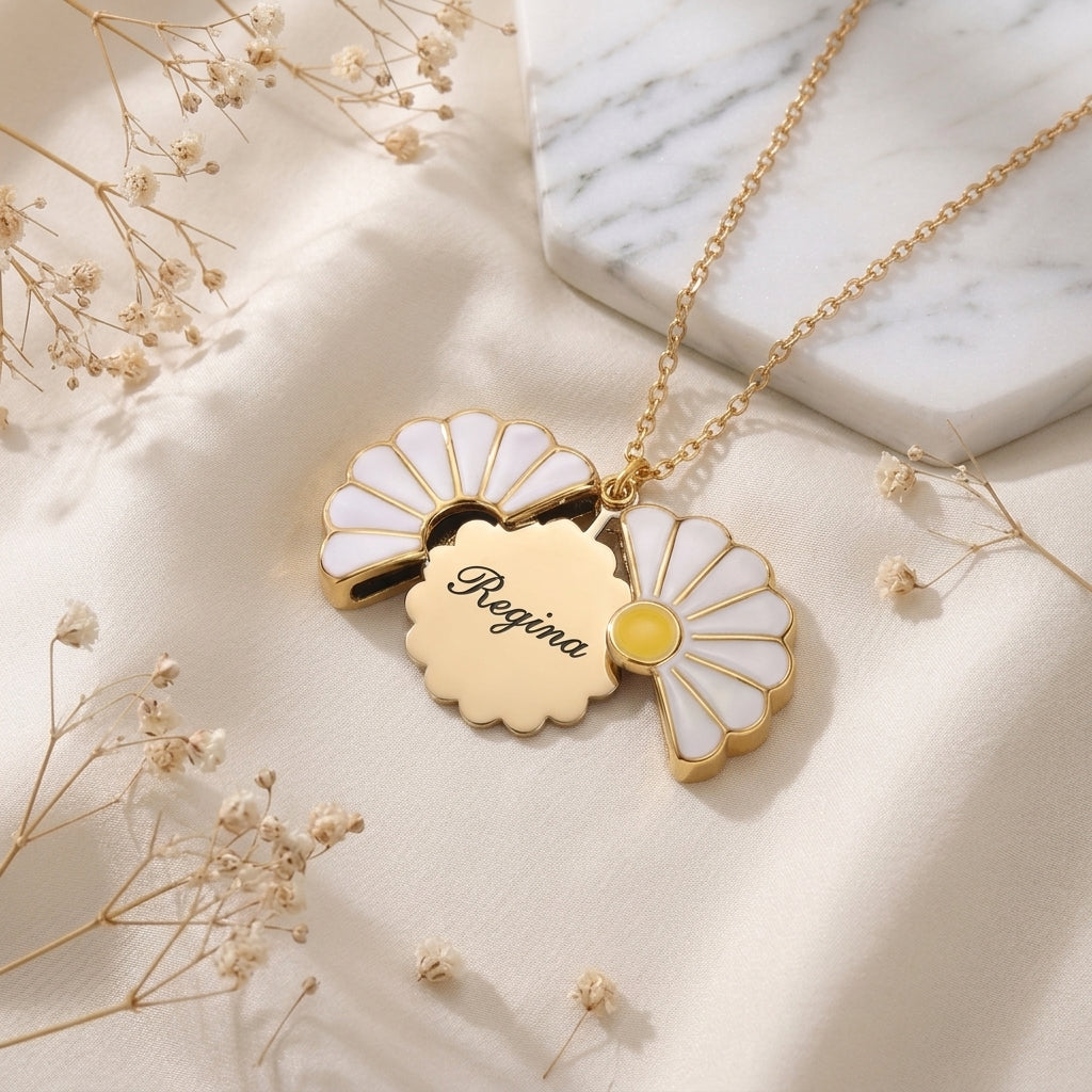 Collier marguerite doré ouvert sur un prénom gravé, posé sur un tissu clair