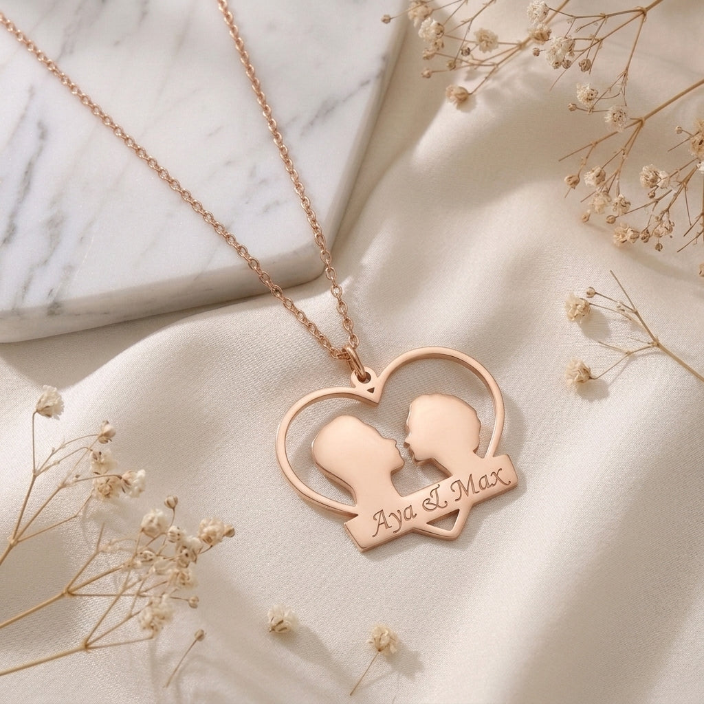 Pendentif couple en or rose posé à plat, deux prénoms gravés sous un cœur