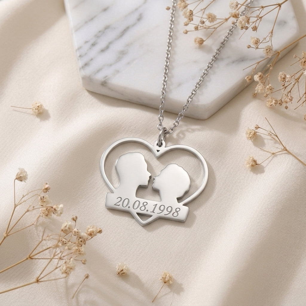 Pendentif couple en acier inoxydable posé à plat, date gravée sous un cœur