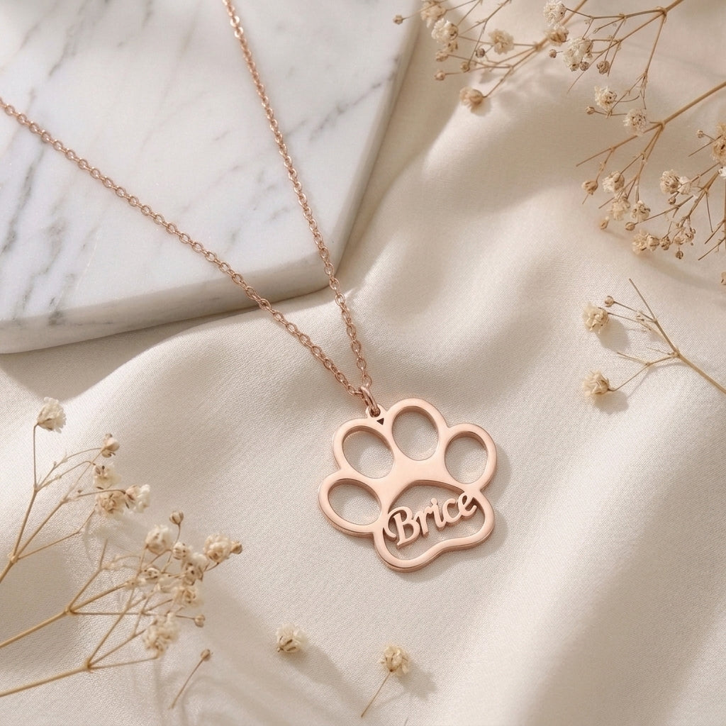 Collier patte d'animal en or rose posé à plat, prénom gravé