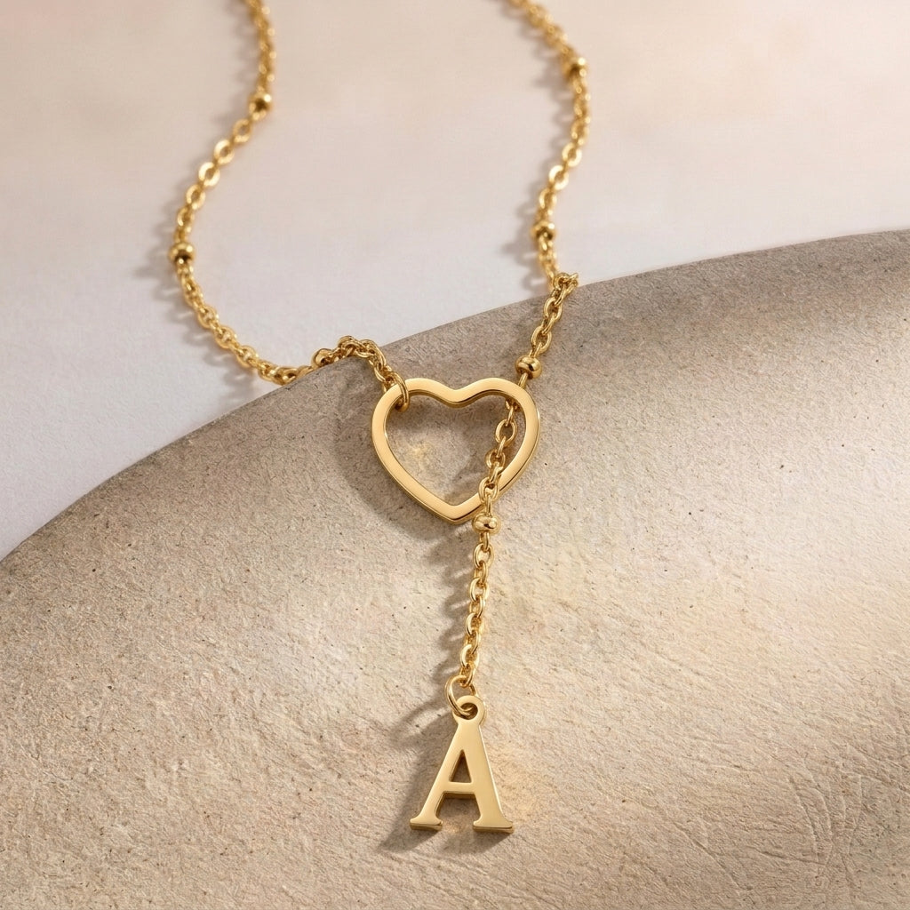 Gros plan sur un collier doré, cœur ajouré et initiale suspendue