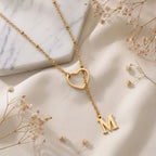 Collier doré à cœur ajouré et initiale gravée, posé à plat