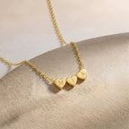 Gros plan sur un collier doré à petits cœurs gravés d'initiales