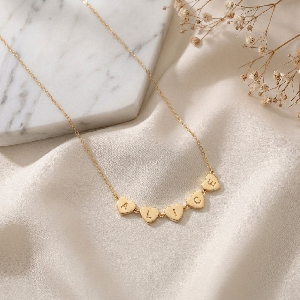 Collier doré à cœurs gravés d'initiales posé à plat sur un tissu clair