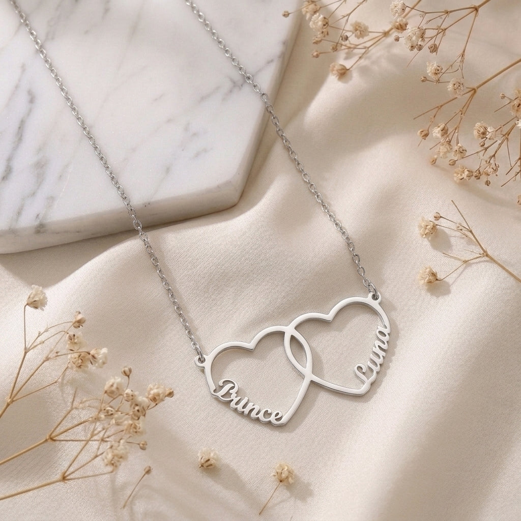 Collier deux cœurs entrelacés en acier inoxydable posé à plat sur un tissu clair