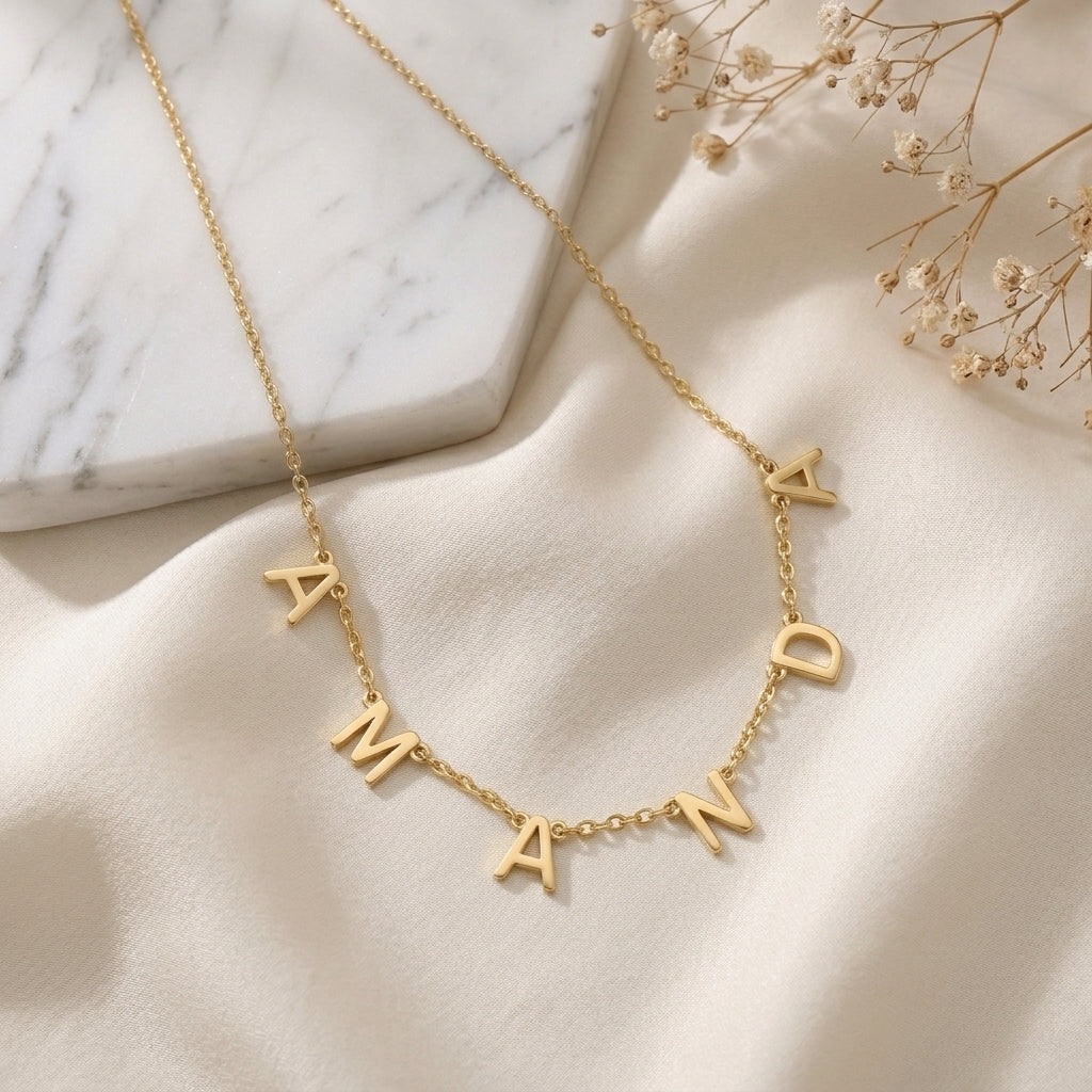 Collier doré à lettres majuscules formant un prénom, posé à plat