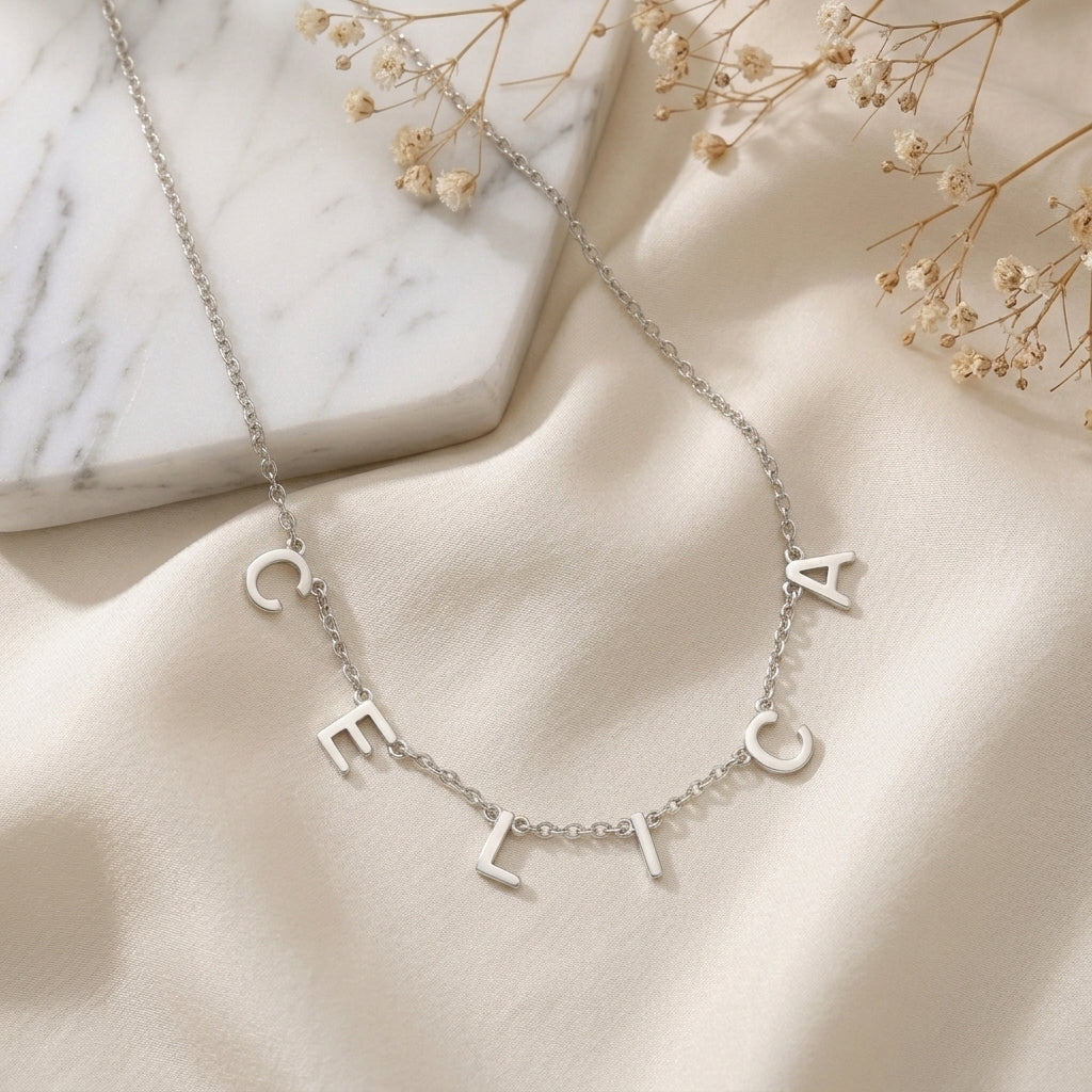Collier en acier inoxydable à lettres majuscules formant un prénom, posé à plat