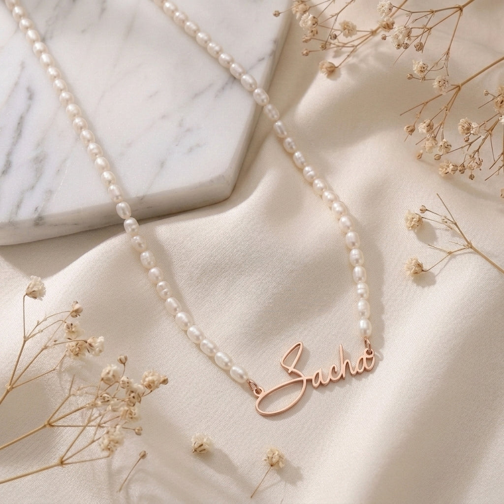 Collier de perles posé à plat, prénom en or rose en écriture manuscrite