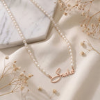 Collier de perles posé à plat, prénom en or rose en écriture manuscrite