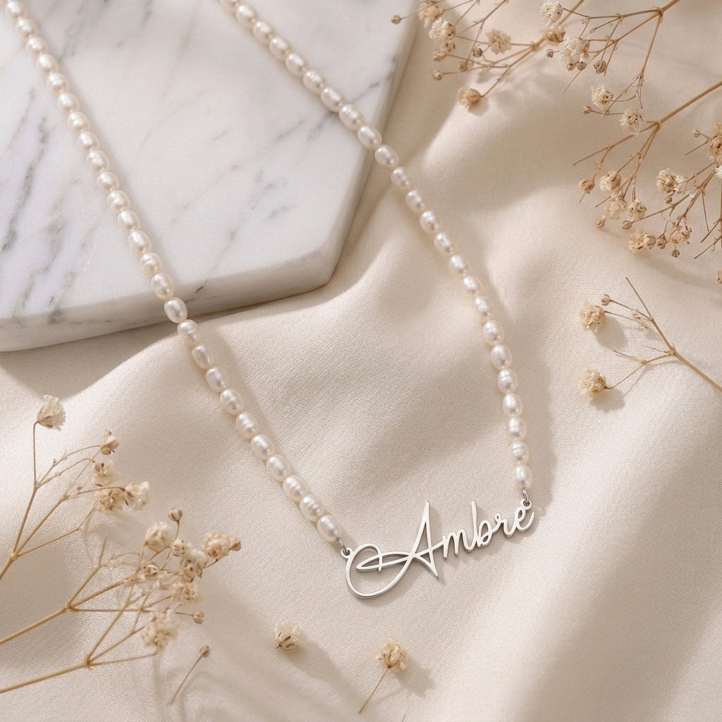Collier de perles posé à plat, prénom en acier inoxydable en écriture manuscrite