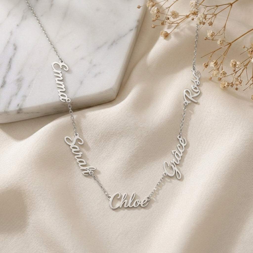 Collier en acier inoxydable à plusieurs prénoms, posé à plat sur un tissu clair