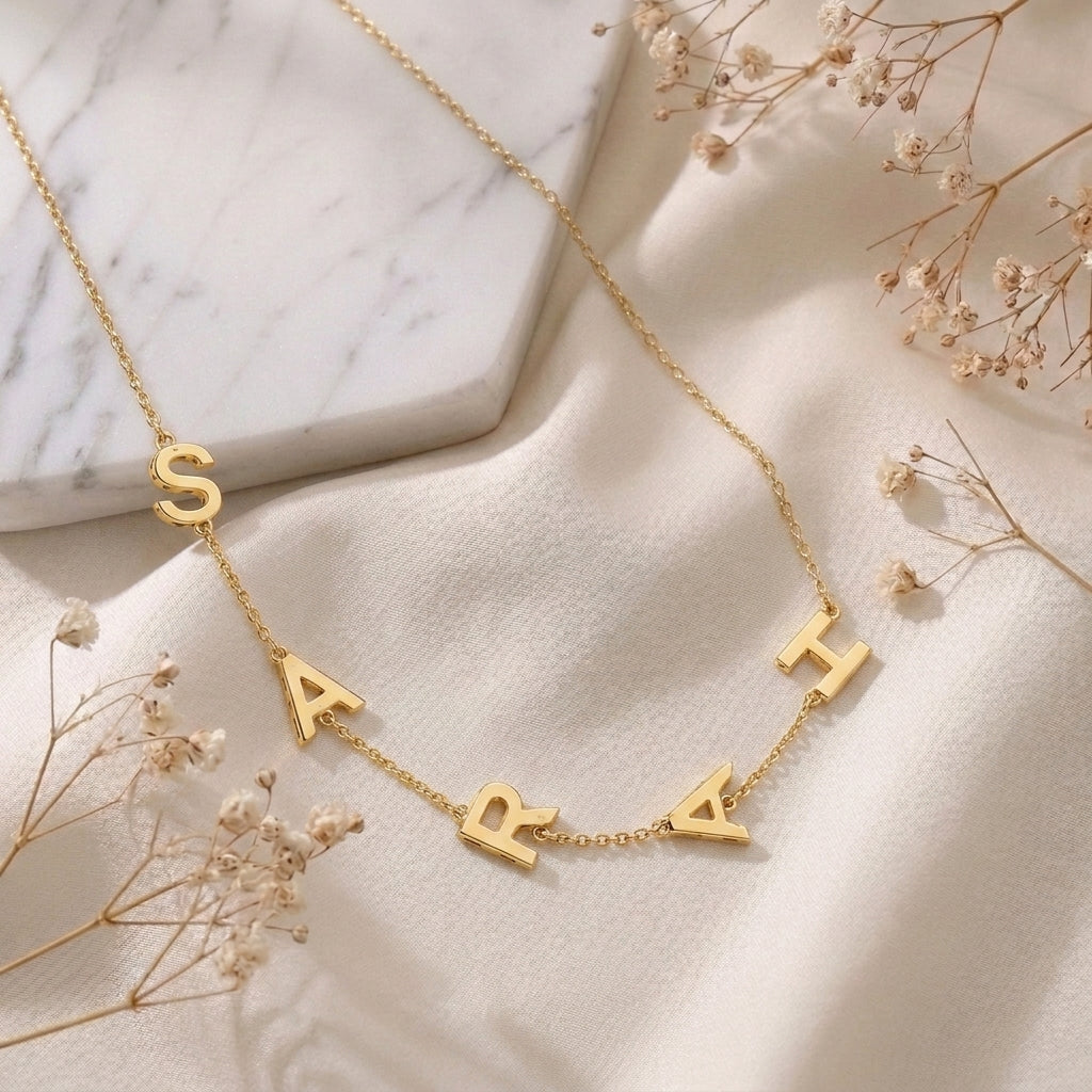 Collier doré aux lettres suspendues posé à plat sur un tissu clair