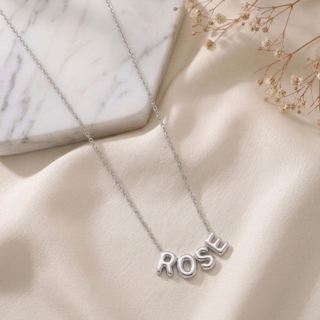 Collier en acier inoxydable à lettres bombées posé à plat sur un tissu clair