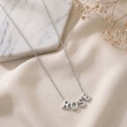 Collier en acier inoxydable à lettres bombées posé à plat sur un tissu clair