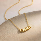 Gros plan sur un collier doré à lettres bombées formant un prénom