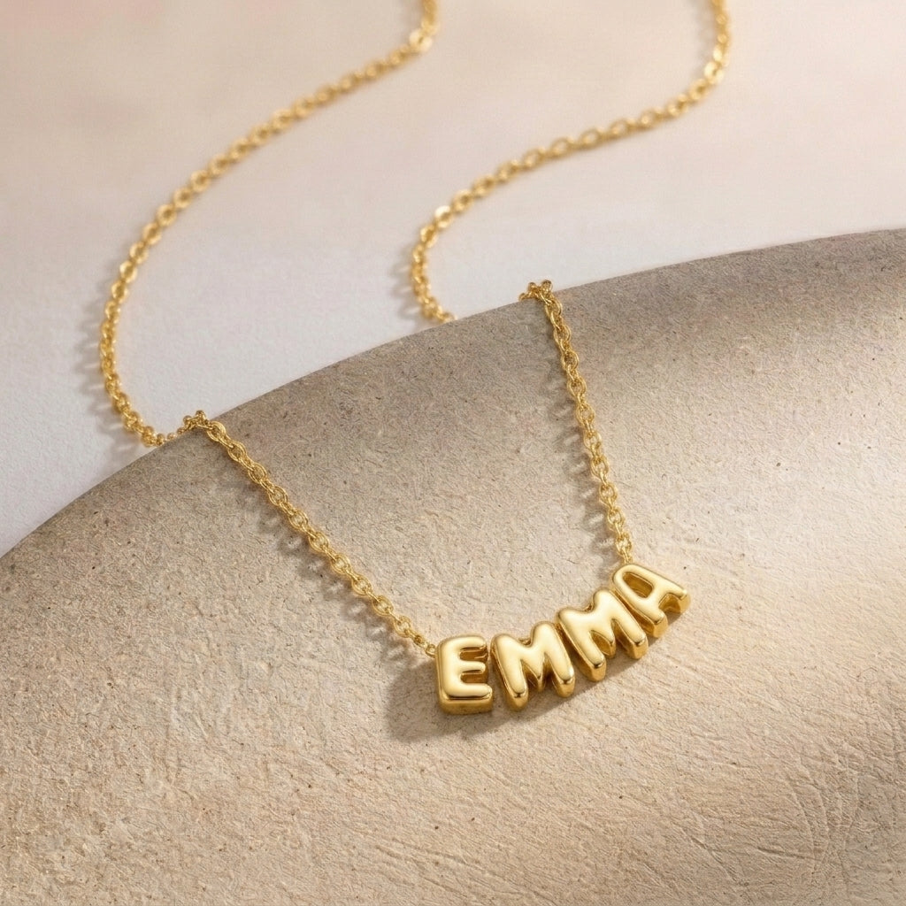 Gros plan sur un collier doré à lettres bombées formant un prénom