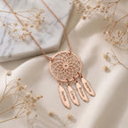 Collier attrape-rêves en or rose posé à plat, plumes gravées de prénoms